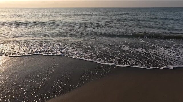 Waves of a calm Mediterranean sea reach the brown sand beach, with a horizon line at sunrise or sunset with a clear sky
