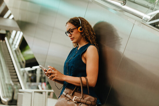 Young woman with headphones checks smartphone during city transit
