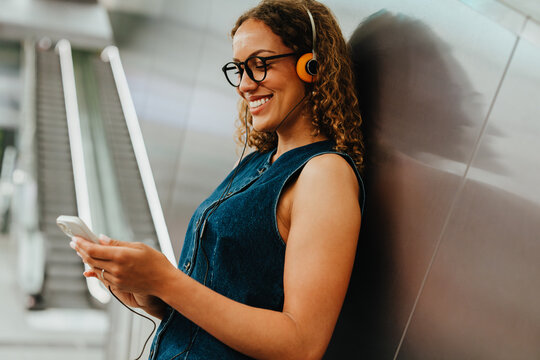 Woman uses smartphone while wearing vintage headphones in urban transit station
