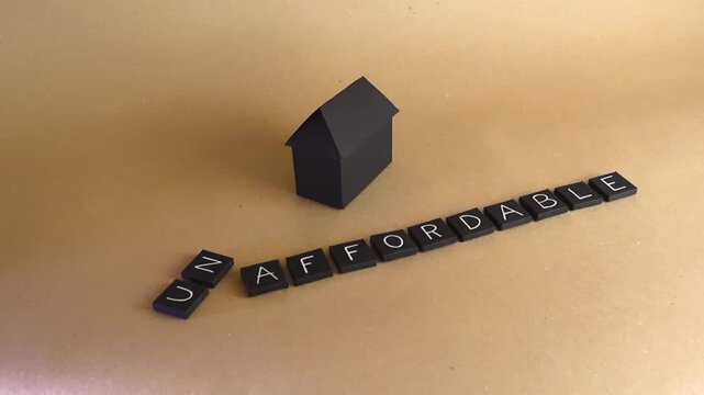 Black paper house model sitting next to letter tiles spelling the word unaffordable, conceptualizing the current housing crisis, high property prices, and expensive mortgage rates