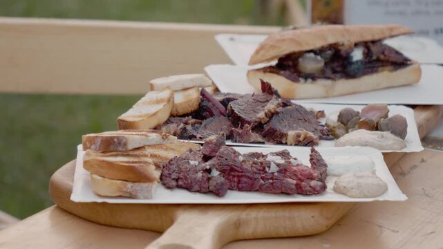 A portion of beef steak is placed on a wooden board with bread and sauces at a lively street food festival in Bukovina. Visitors enjoy the food and atmosphere.