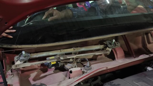 Mechanic removes damaged front windshield from car at automotive repair garage. Footage shows windshield replacement and auto glass repair process, highlighting vehicle maintenance