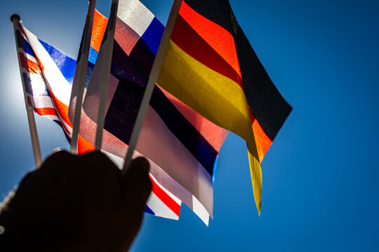 German colors glow beside neighboring flags as the sun breaks through. The handheld display captures motion pride and international goodwill beneath a pristine sky