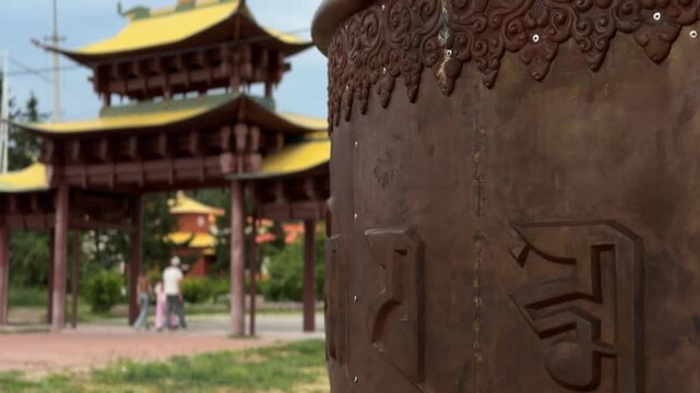 Verkhnyaya Ivolga, Russia - July 23, 2026: Ornate Tibetan prayer wheel stands prominently with traditional pagoda structures and greenery visible in the serene landscape