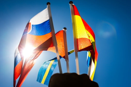 A burst of sun pierces through fluttering flags in a clear blue sky The handheld poles carry colors of European nations celebrating outdoor spirit travel unity pride and energy