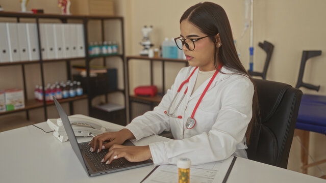Young hispanic doctor at desk with stethoscope holding lower back for backache in medical building; work fatigue.