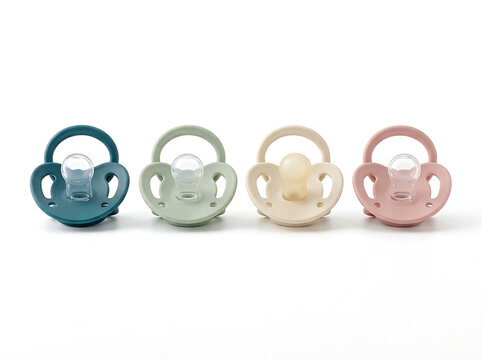 Collection of matte newborn baby pacifiers in trendy muted colors organized neatly on a plain white studio setting.