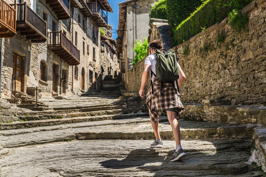 Young male tourist walking along medieval stone street in Rupit village, Catalonia, Spain, exploring historic architecture and authentic