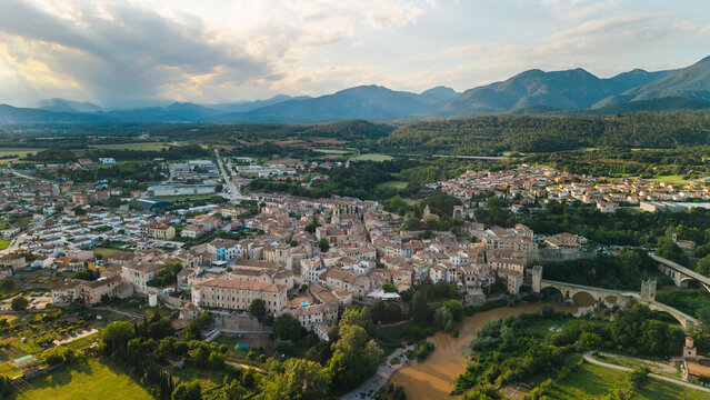 Aerial panoramic view of Besalu medieval town and iconic stone bridge in Catalonia Spain with mountains and dramatic sunset 