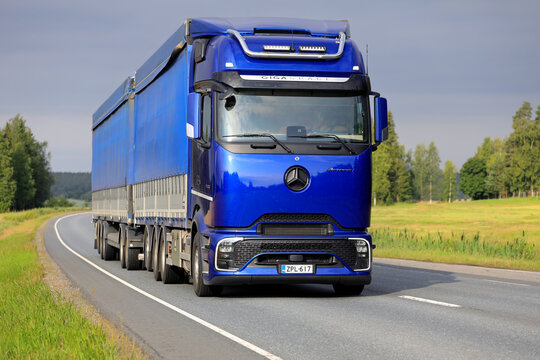 Blue Mercedes-Benz Actros L GigaSpace ProCabin semi-truck hauling double tarp top trailer on morning highway. 