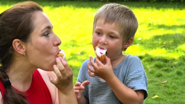 Mother and young son eat ice cream together in a summer park, happy family moment, sweet treat, childhood joy, outdoor leisure.