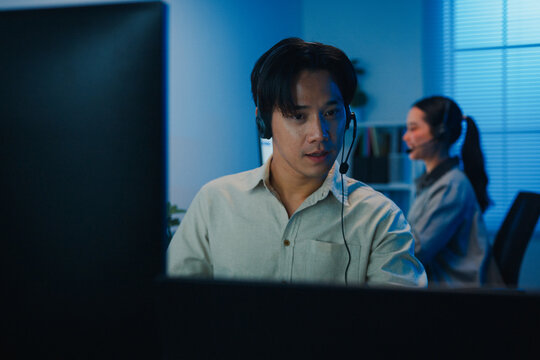 Gen z Asia young call center team or customer support service executive use computer and microphone headset work technical e commerce support in late night office. Telemarketing or sales job concept.