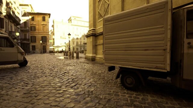 wide cobbled foreground leading to sunlit square, low viewpoint emphasizes pattern and scale, classical building bases frame distant urban life and travel