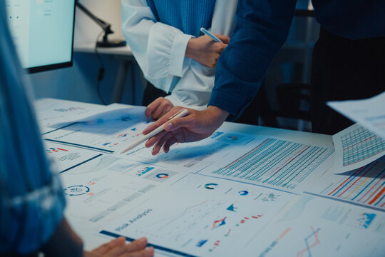 Close up Asia businesspeople meeting plan analysis statistics brainstorm and work with paperwork around table in office conference room at night. Business finance partners strategy investment success.