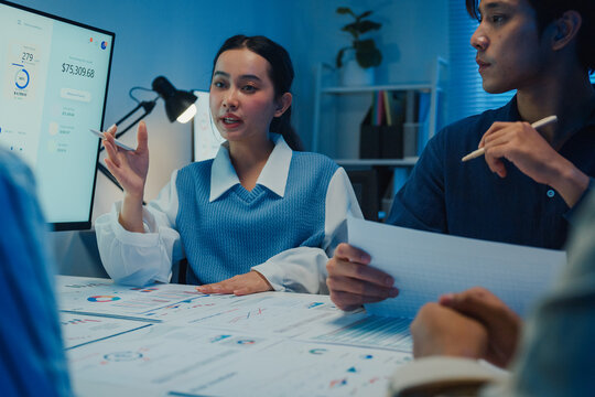 Asia businesspeople presentation sales meeting plan statistics brainstorm and work with paperwork around table in office conference room at night. Business finance partner strategy investment success.