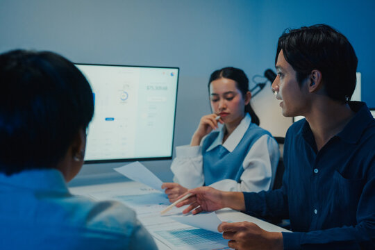 Asia businesspeople presentation sales meeting plan statistics brainstorm and work with paperwork around table in office conference room at night. Business finance partner strategy investment success.