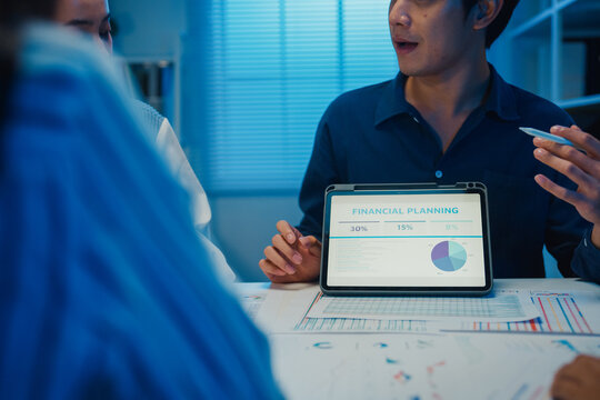 Startup Asia businesspeople meeting plan analysis statistics brainstorm and tablet point graph chart employee take note in office conference room at night. Business finance partners strategy success.