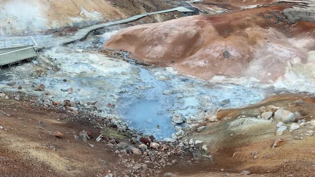 Iceland. Colorful geothermal landscape with steaming blue water and mineral-rich earth, showcasing a series of rocky formations and wooden walkways in a natural hot spring area