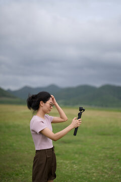 Woman with windblown hair filming with a gimbal in a green field