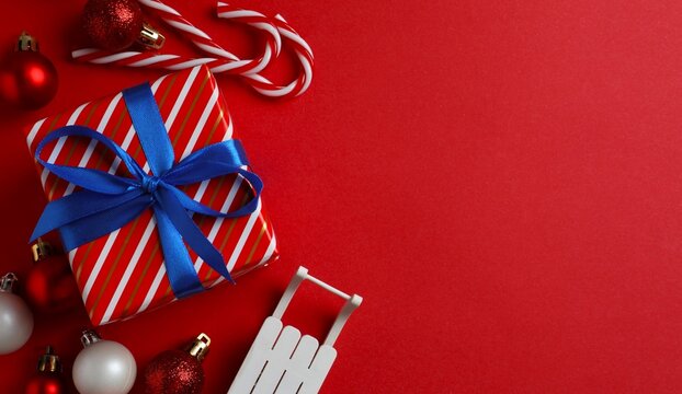 Beautiful gift box tied with blue bow and Christmas decorations on red background 