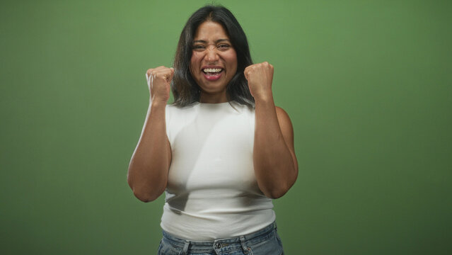 Woman clenches fists and screams in studio wearing white tank top and jeans; triumph victory empowerment.
