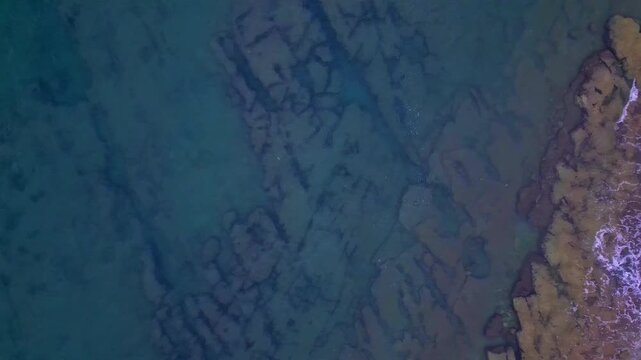 The waves crash against the rocky coastline, showcasing a dramatic seaside landscape. The aerial view reveals the intricate patterns of nature's artistry, where the beach meets the ocean's edge.