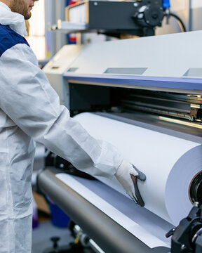Adult Man Operating Large Printing Machine In Industrial Workshop With Paper Roll