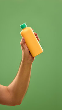 Hand presenting yellow skincare bottle with turquoise cap on green background. Concept of outdoor skincare, summer beauty essentials, and sun protection.