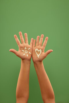 Two children hands displaying skincare cream swatches on palms against green background. Concept of cosmetic testing, moisturizing skincare routine, and product comparison.
