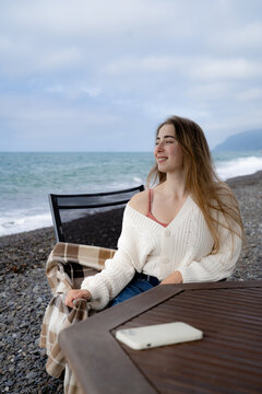 Young woman sitting by the sea and looking into the distance, enjoying a quiet coastal getaway on a cloudy day.