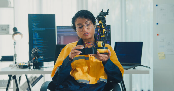 Young African American female robotics engineer discussing mechanical part on video call and looking at camera in laboratory. Remote work, virtual training, online meeting, future technology concept.