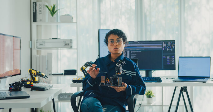 Young African American female robotics engineer discussing mechanical part on video call and looking at camera in laboratory. Remote work, virtual training, online meeting, future technology concept.