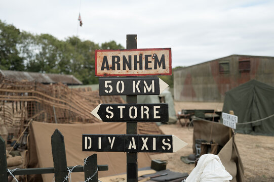 Shallow focus of a WW2 era had hot sign for the famous town of Arnhem. The camp shows a reenactment of the British Parachute regiment. Showing signs to the stores and distance to the Arnhem bridge.