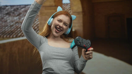 Woman holding a gamepad and wearing cat ear headphones makes rock horns gesture in building  joy celebration. © Krakenimages.com