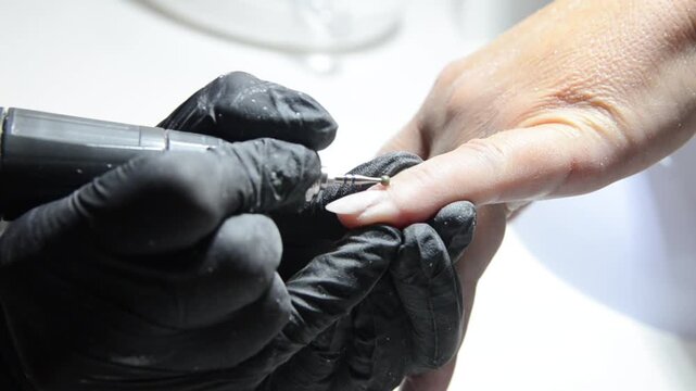 Manicurist uses a ball drill bit to treat the cuticle area during professional hardware manicure. Close-up nail care procedure in a beauty salon.