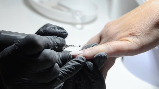 Manicurist uses a ball drill bit to treat the cuticle area during professional hardware manicure. Close-up nail care procedure in a beauty salon.