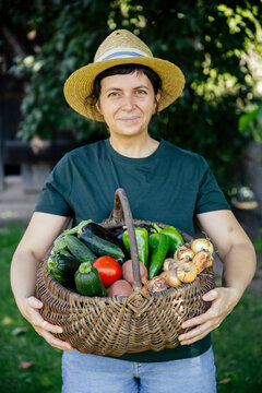 Person holding fresh harvest of garden-grown vegetables, including tomatoes, cucumbers, peppers, potatoes, and onions
