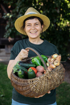 Person holding fresh harvest of garden-grown vegetables, including tomatoes, cucumbers, peppers, potatoes, and onions