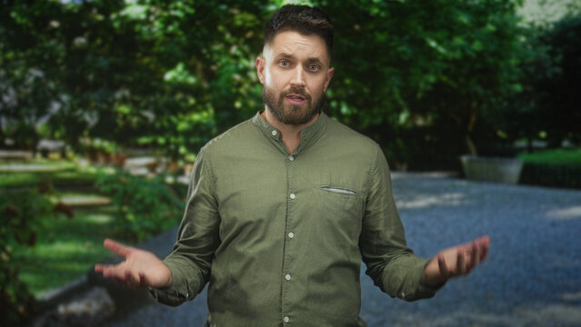 Man with beard showing palms up and open hands, smiling with eyes closed on a forest pathway in daylight; serenity openness.