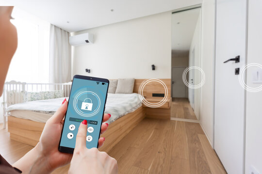 Close up smartphone in female hand with smart home system app interface on cellphone screen, young woman controlling all house system by phone in modern apartment, internet of things concept.