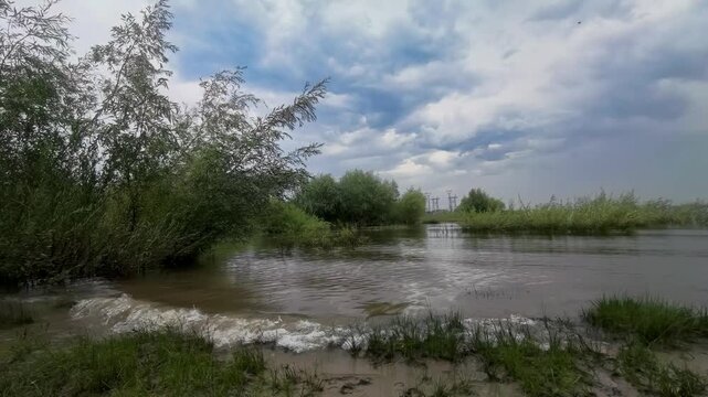 Flooded riverbank lies under dramatic storm clouds, high water, severe weather, overcast landscape, natural flooding after heavy rain.