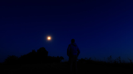 Silhouette of a person in nature observing night sky, Moon, stars and planets from a remote location. © astrosystem
