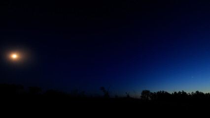 Moon on a twilight sky with stars, planets and landscape mountain silhouettes. © astrosystem