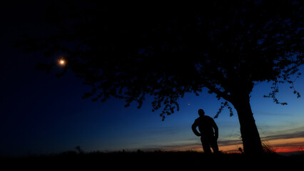 Silhouette of a person in nature observing night sky, Moon, stars and planets from a remote location. © astrosystem