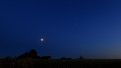 Moon on a twilight sky with stars, planets and landscape mountain silhouettes. © astrosystem