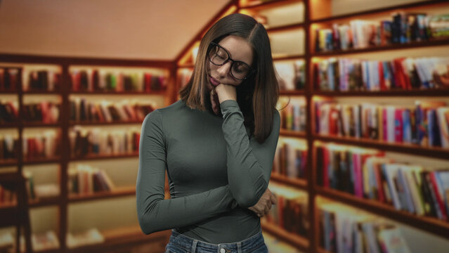 Young woman resting chin on hand wearing glasses and a turtleneck, standing among packed bookshelves in a library; pensive study reflection.
