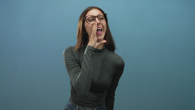 Woman cupping hand to mouth and shouting in studio, wearing glasses and turtleneck; urgent announcement.