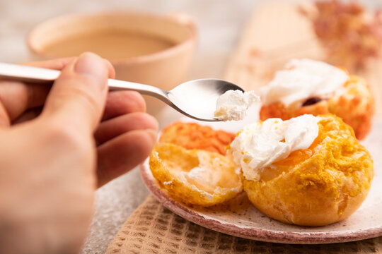 Сhoux pastry cake with cup of coffee with hand on brown concrete, close up, side view, selective focus.