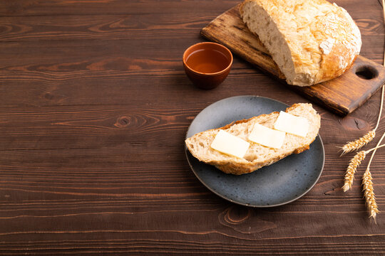 Slice of homemade bread with butter on plate on brown wooden, copy space, side view.