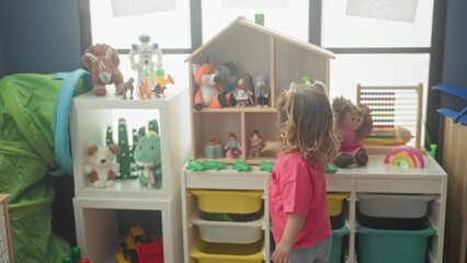 Little girl in pink shirt holds toy scissors beside wooden dollhouse in a bright playroom  curiosity imagination. © Krakenimages.com